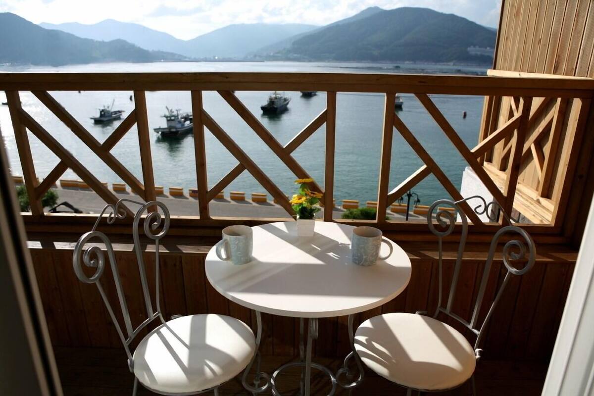 A balcony with a view of boats on a lake, a table with two chairs, and a wooden railing.