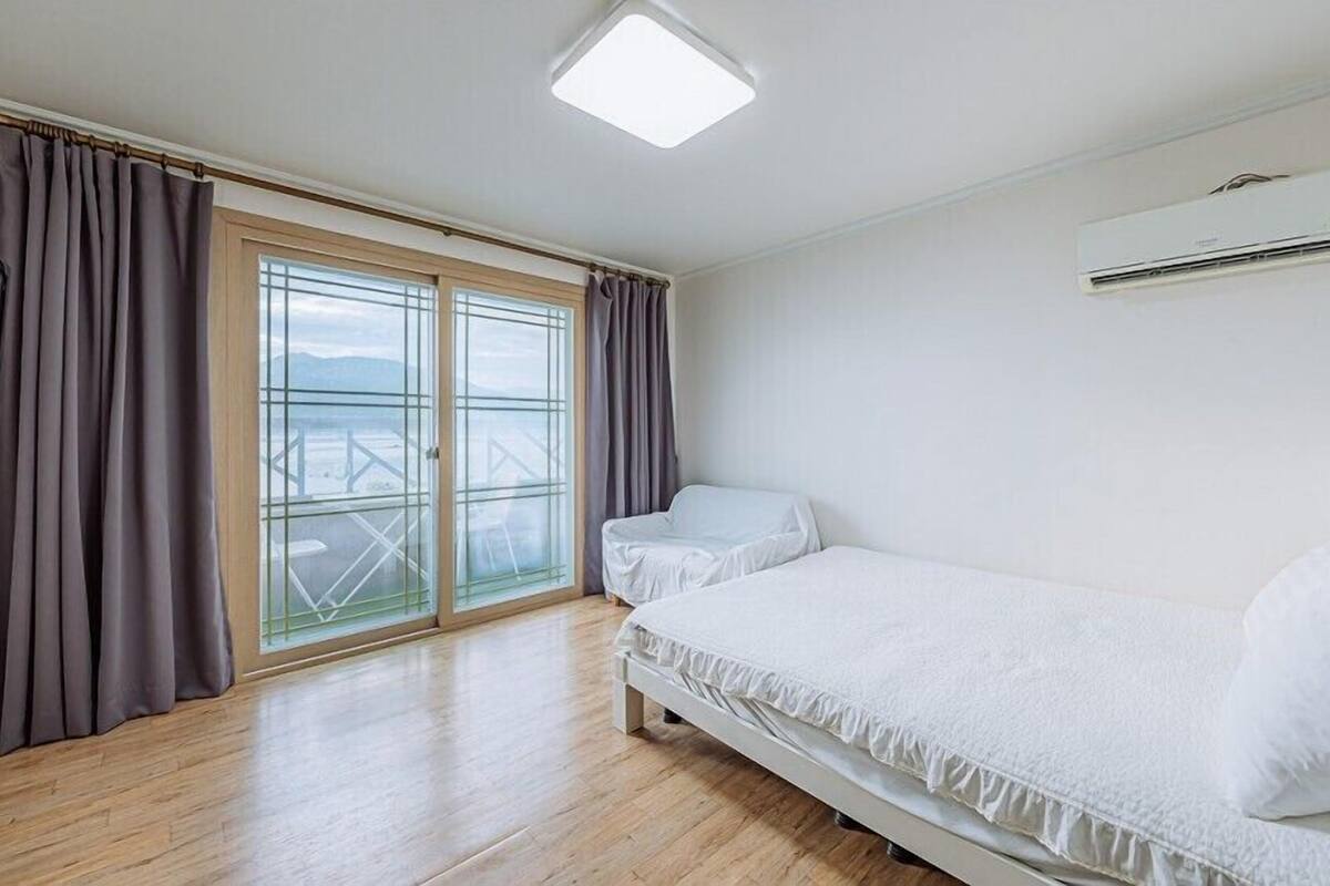 A bedroom with a bed, a window with curtains, and an air conditioning unit.