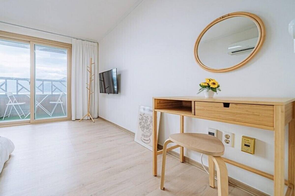 A hotel room with a bed, a desk with a chair, a TV, and a balcony with a view.
