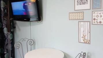 A room with a flat-screen TV mounted on the wall, a round table with two chairs, and various framed artworks on the wall.