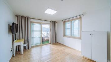 Een kamer met een houten vloer, een wit bureau met stoel, een aan de muur bevestigde televisie, een schuifdeur naar een buitenruimte en een witte kledingkast.