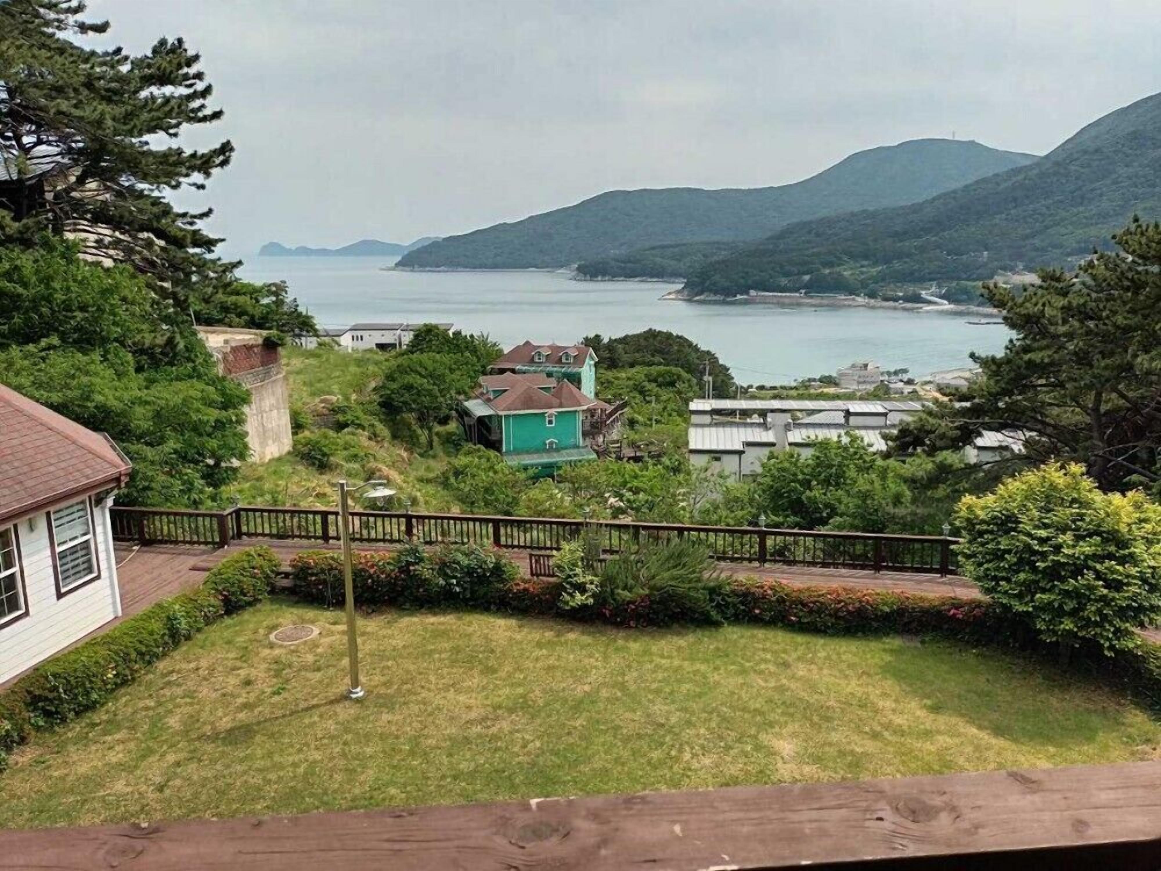 Zona residencial amb cases, un jardí amb gespa i una vista d'un conjunt d'aigua i turons a la distància.