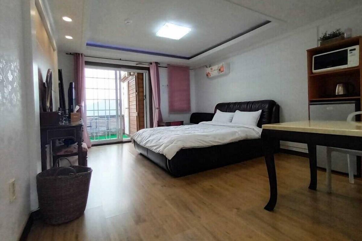 A bedroom with a bed, a desk, a chair, a TV, and a window with curtains.