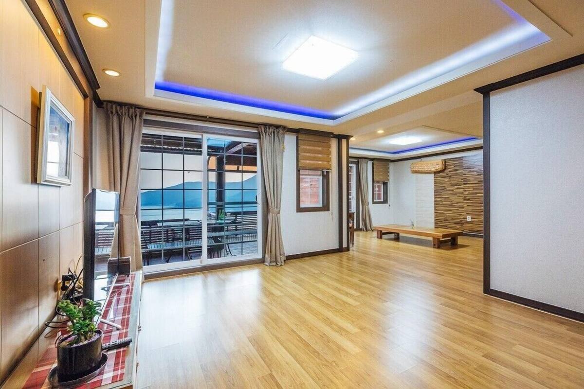 A spacious room with a wooden floor, large sliding glass doors leading to a balcony, and a bench in the corner.