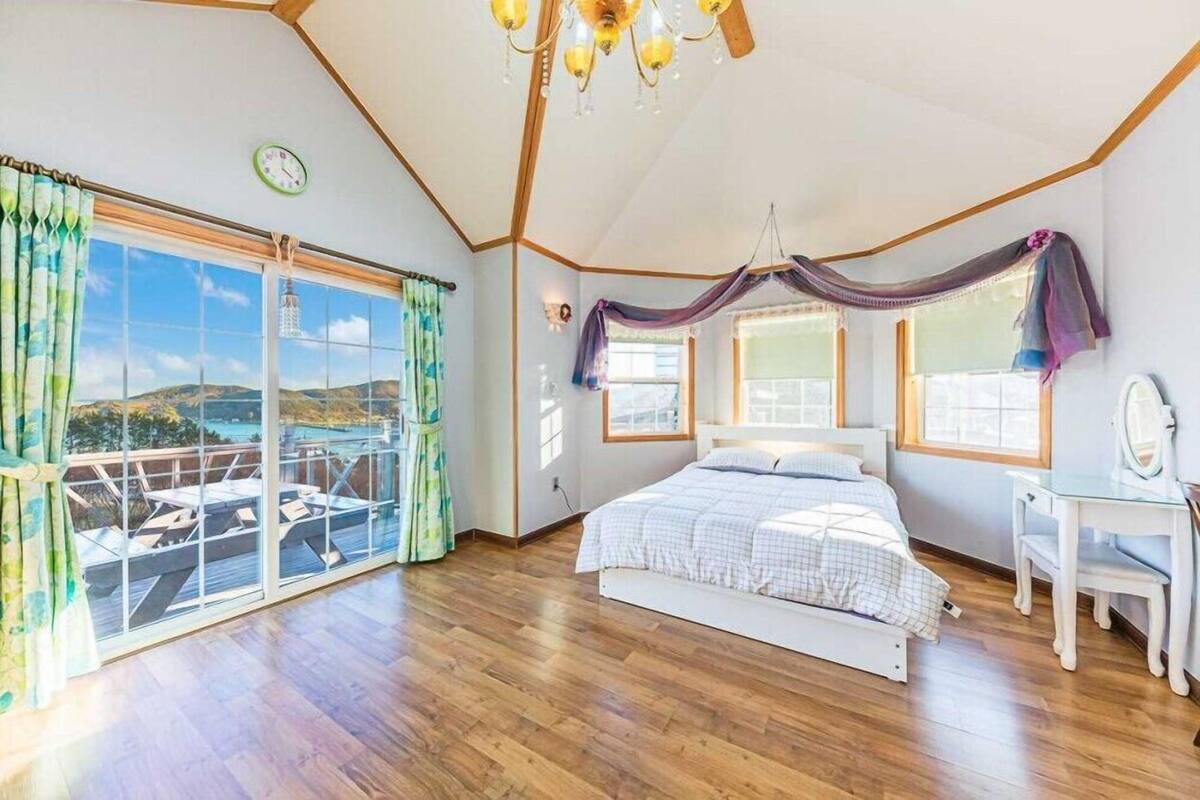 A bedroom with a large bed, a desk, and a view of the outdoors.