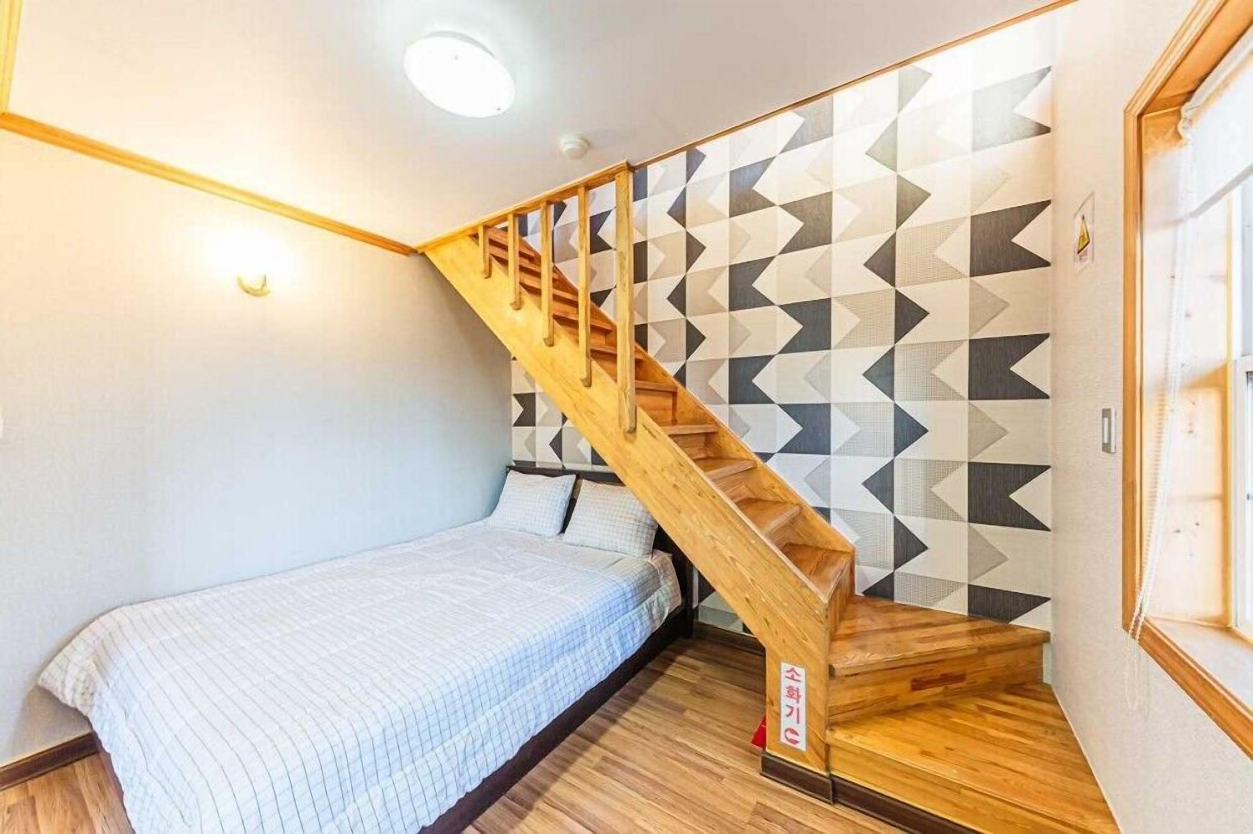 Un dormitorio con una escalera de madera, una cama con colcha a rayas y una pared con estampado geométrico.