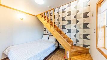 Un dormitorio con una escalera de madera, una cama con colcha a rayas y una pared con estampado geométrico.