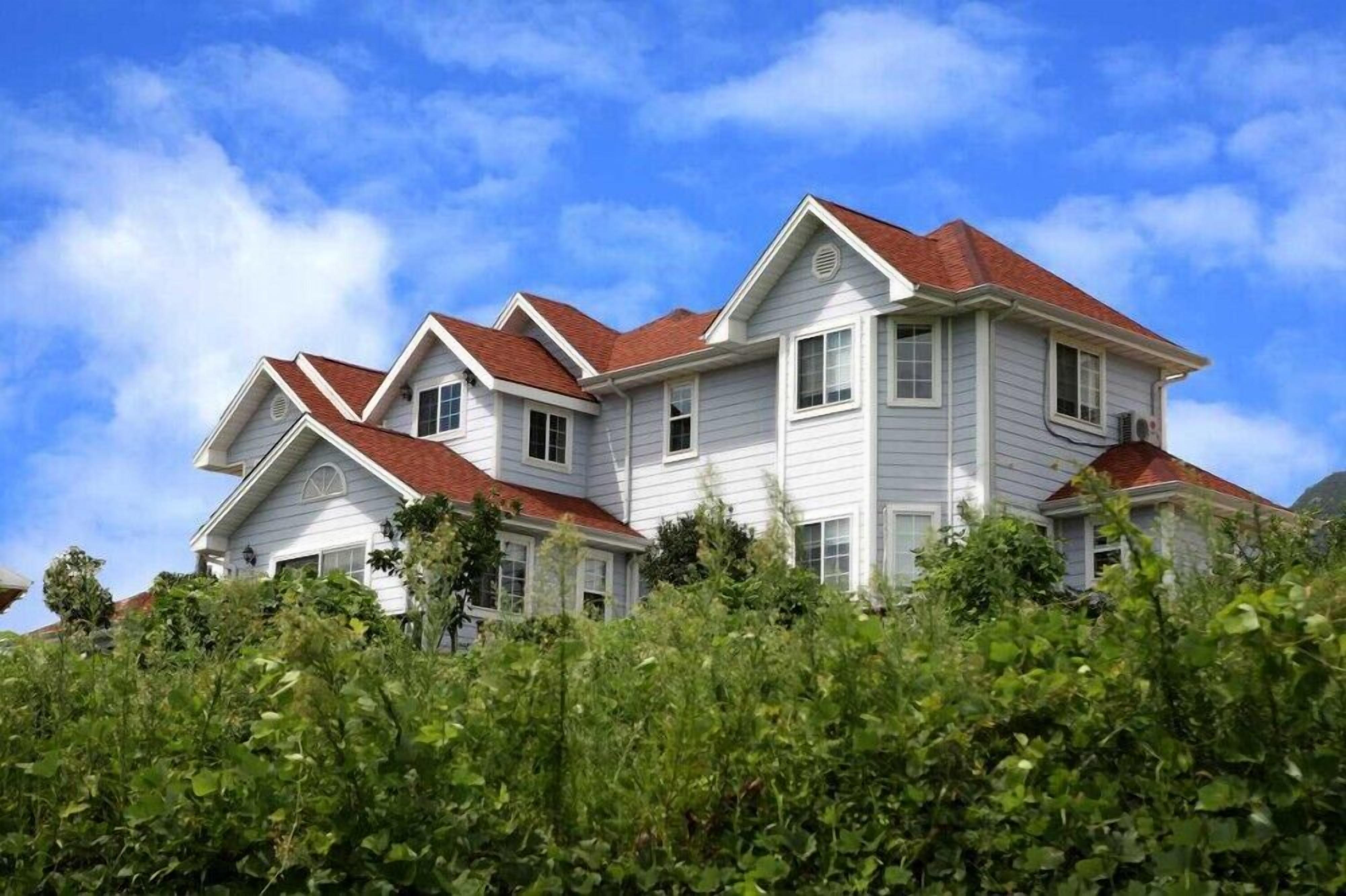 A two-story house with a red roof, white siding, and multiple chimneys.