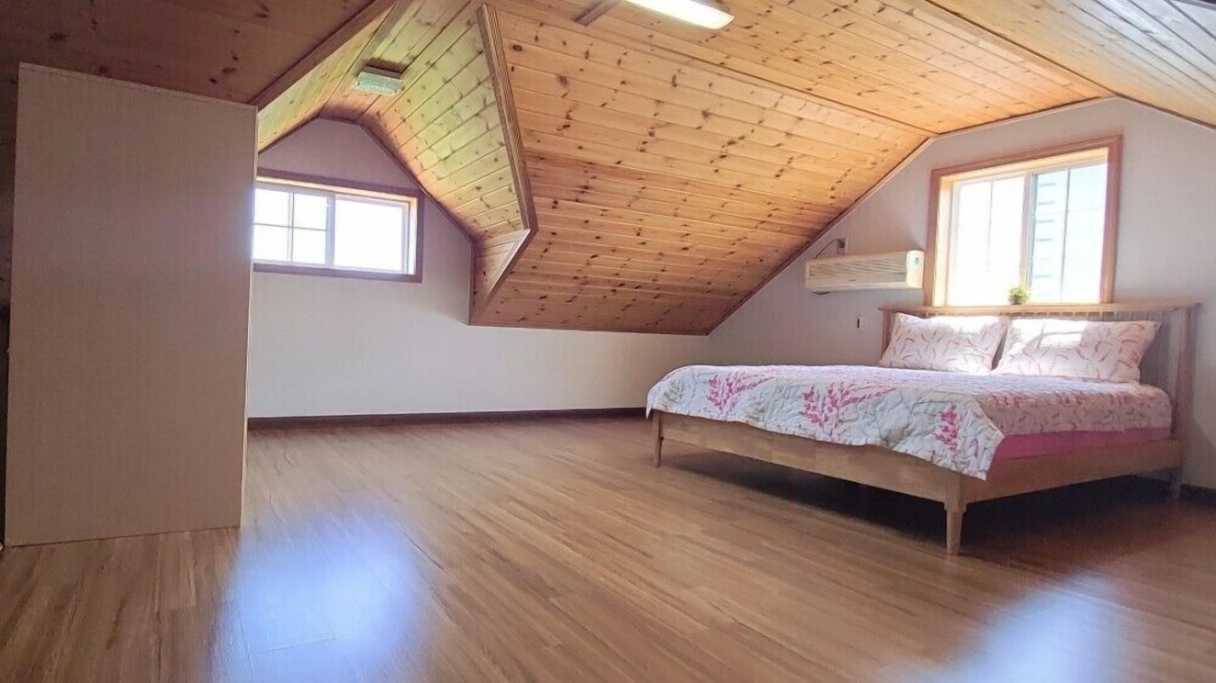 Un dormitorio con techo inclinado, suelo de madera, cama con ropa de cama floral y dos ventanas.