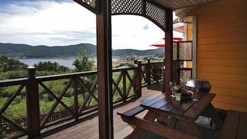 Um deck de madeira com mesa e cadeiras, com vista para um lago e colinas.