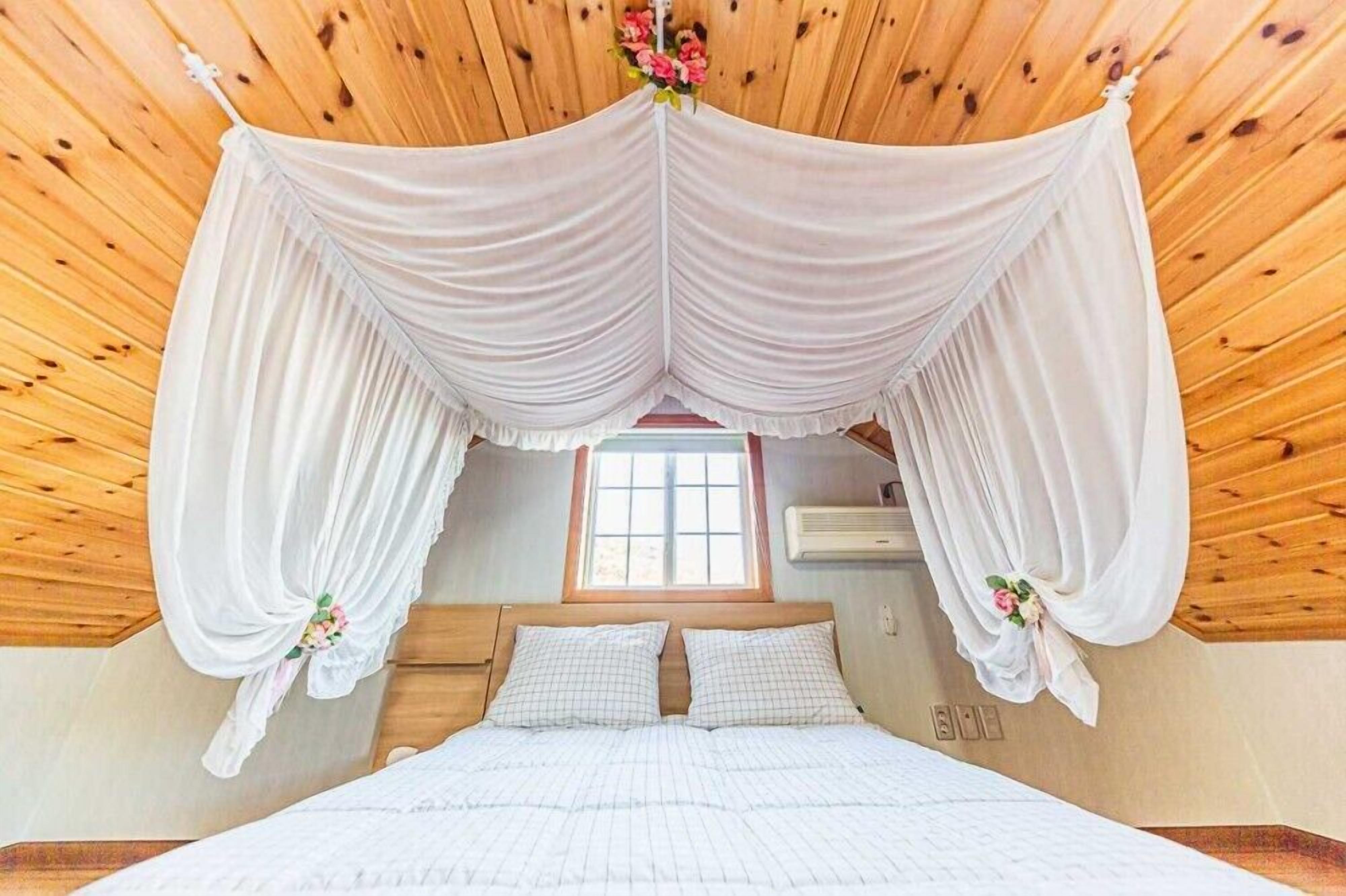 A bedroom with a canopy bed, wooden ceiling, and a window with a view.