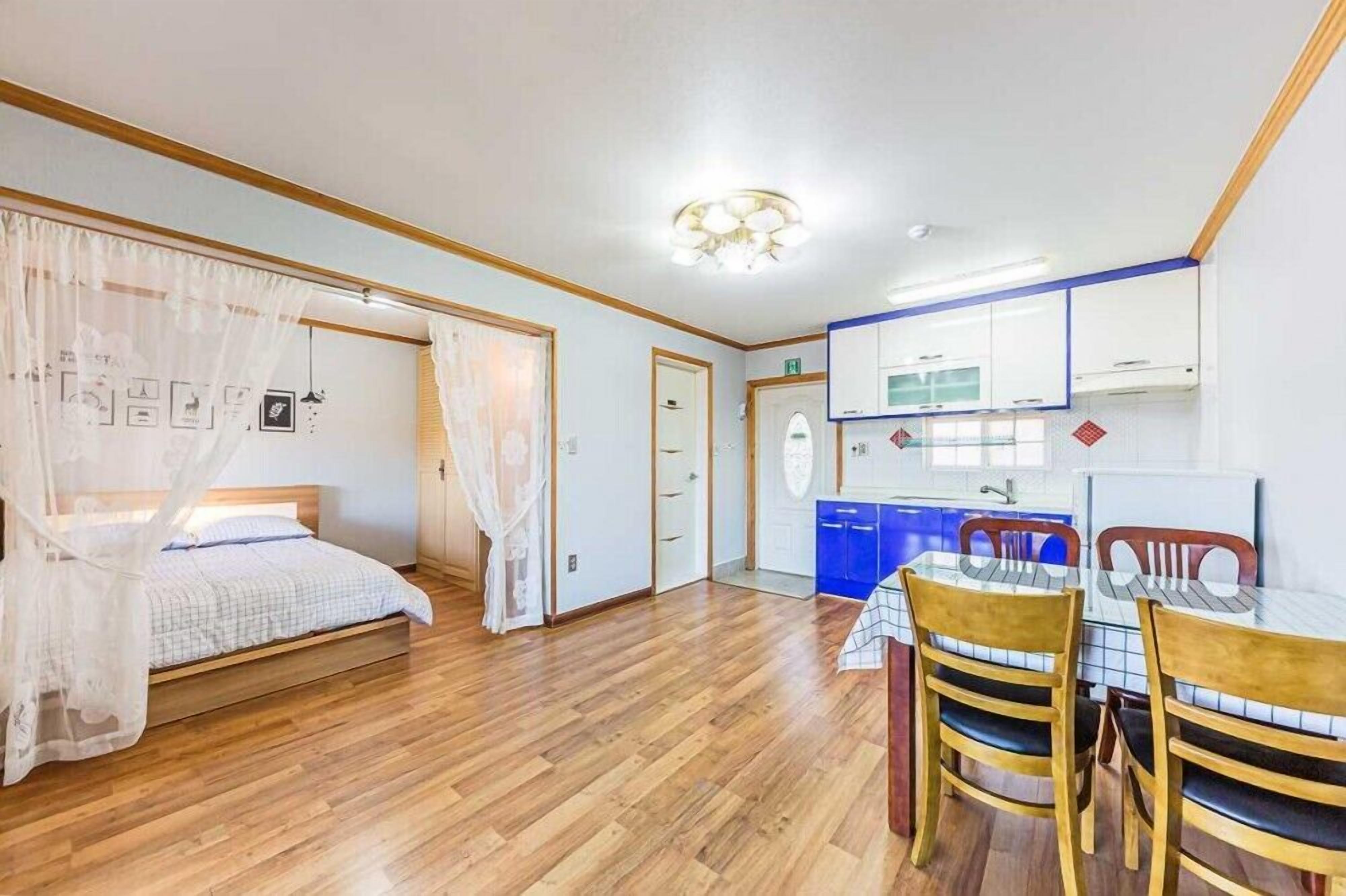 Un dormitorio con cama, mesita de noche y estante. Se observa una ventana con cortinas y un estante fijado a la pared.