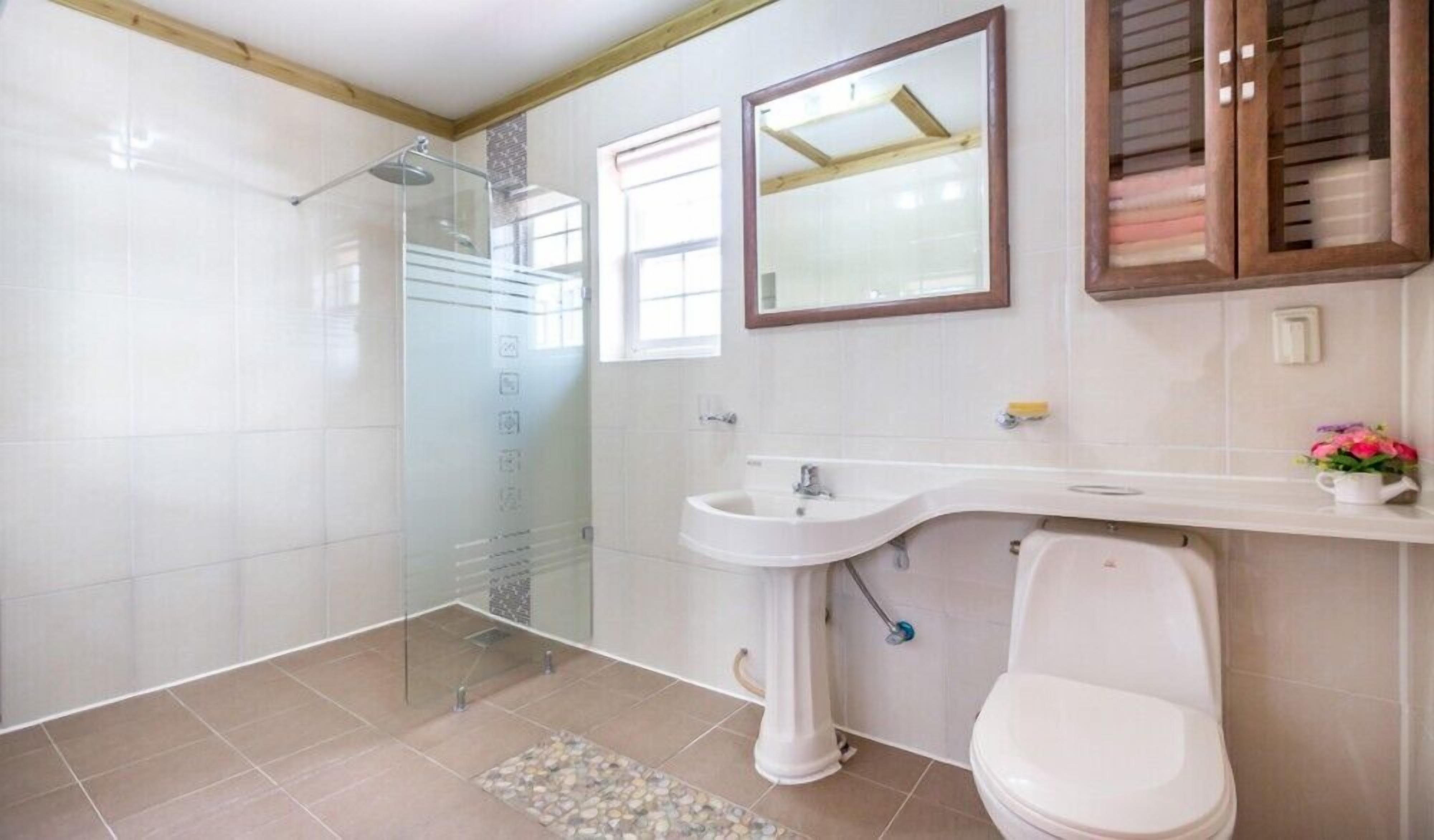 A bathroom with a shower, sink, toilet, and a mirror.