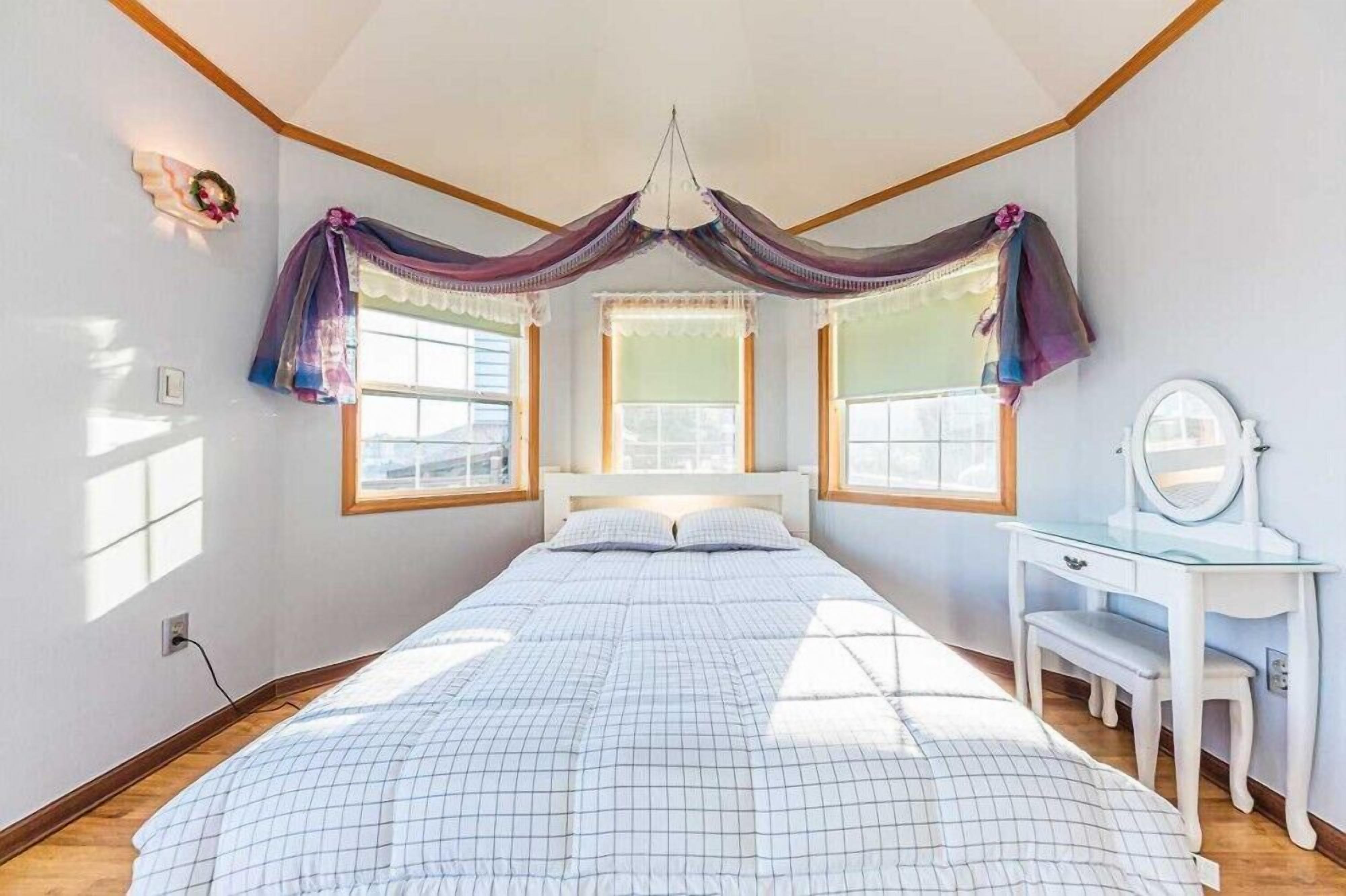 A bedroom with a bed, a nightstand, a dresser, and a window with curtains.
