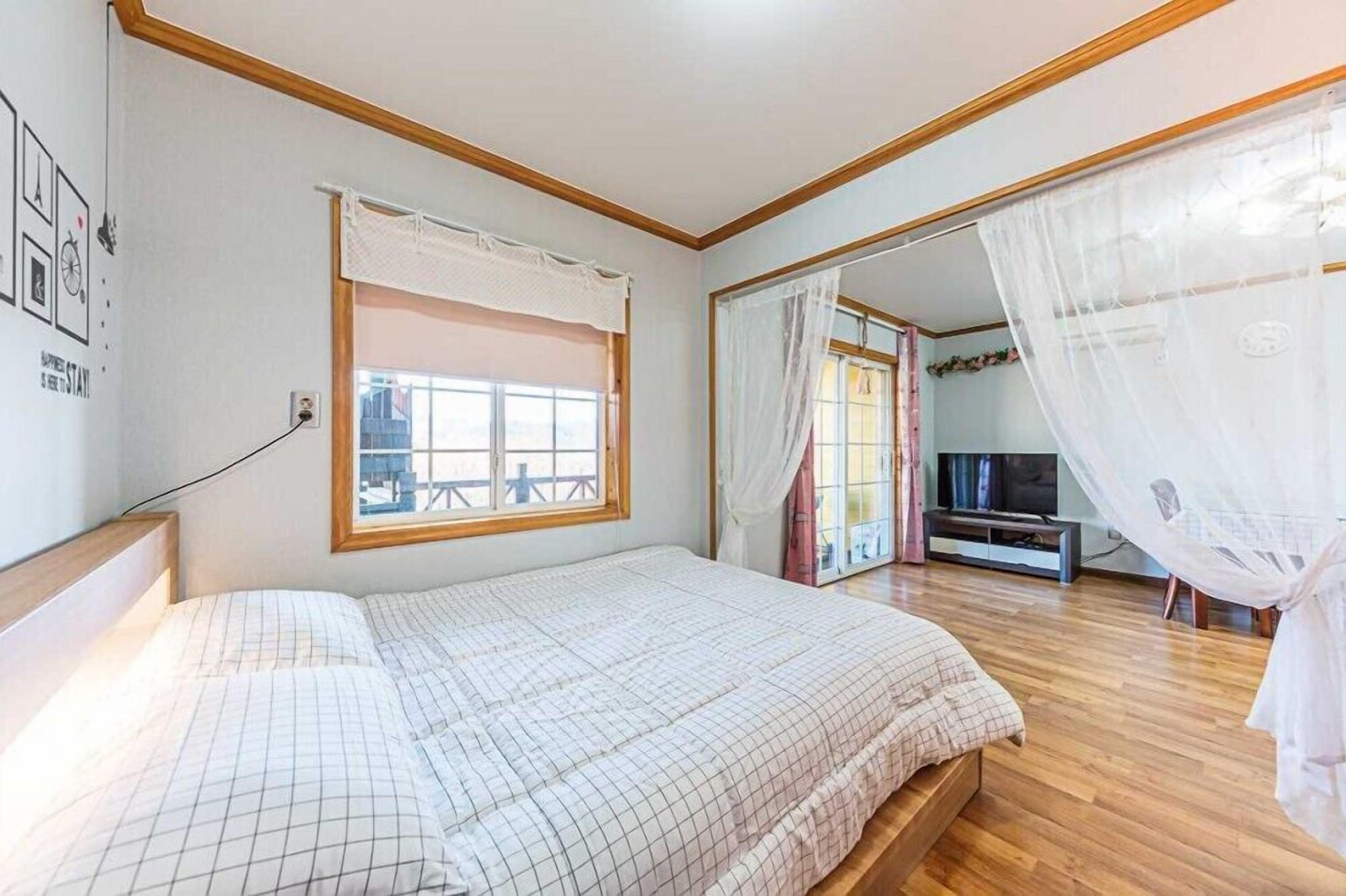 A bedroom with a bed, a window, a TV, and a balcony.