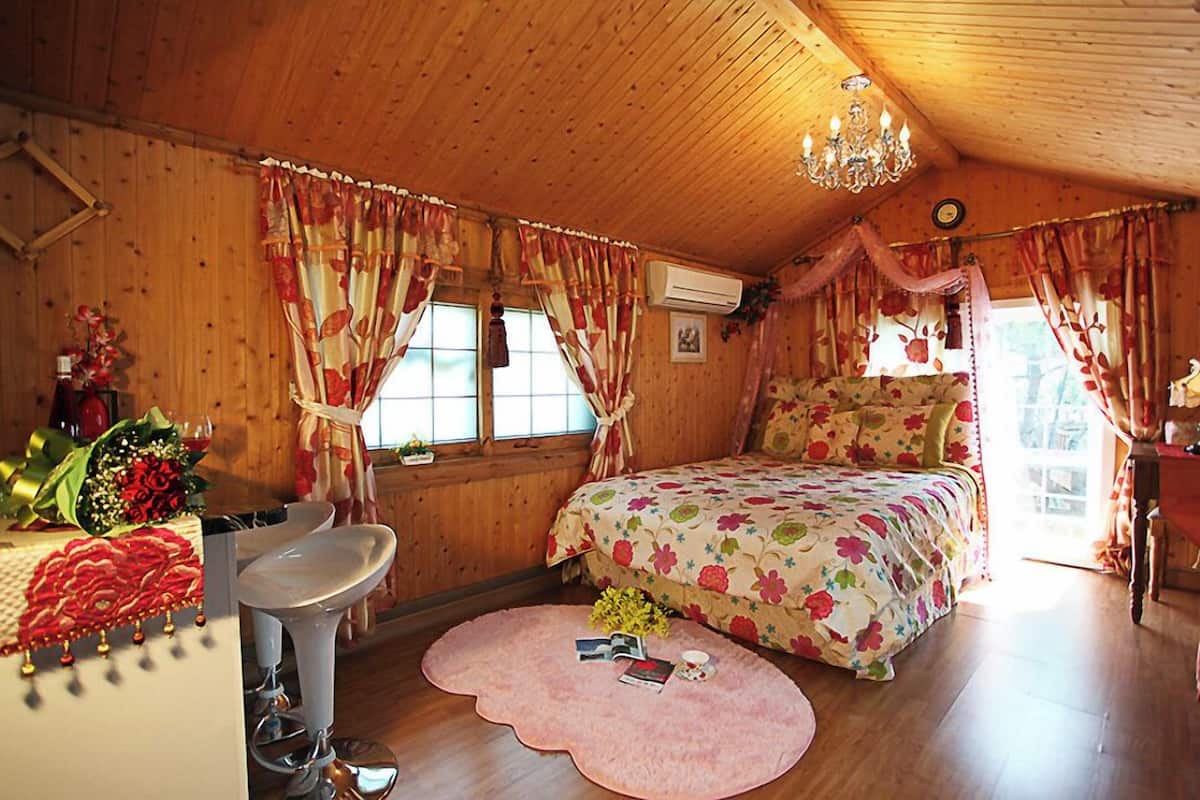 Un dormitorio acogedor con techo de madera, cama con ropa de cama floral, tocador con espejo y alfombra rosa.