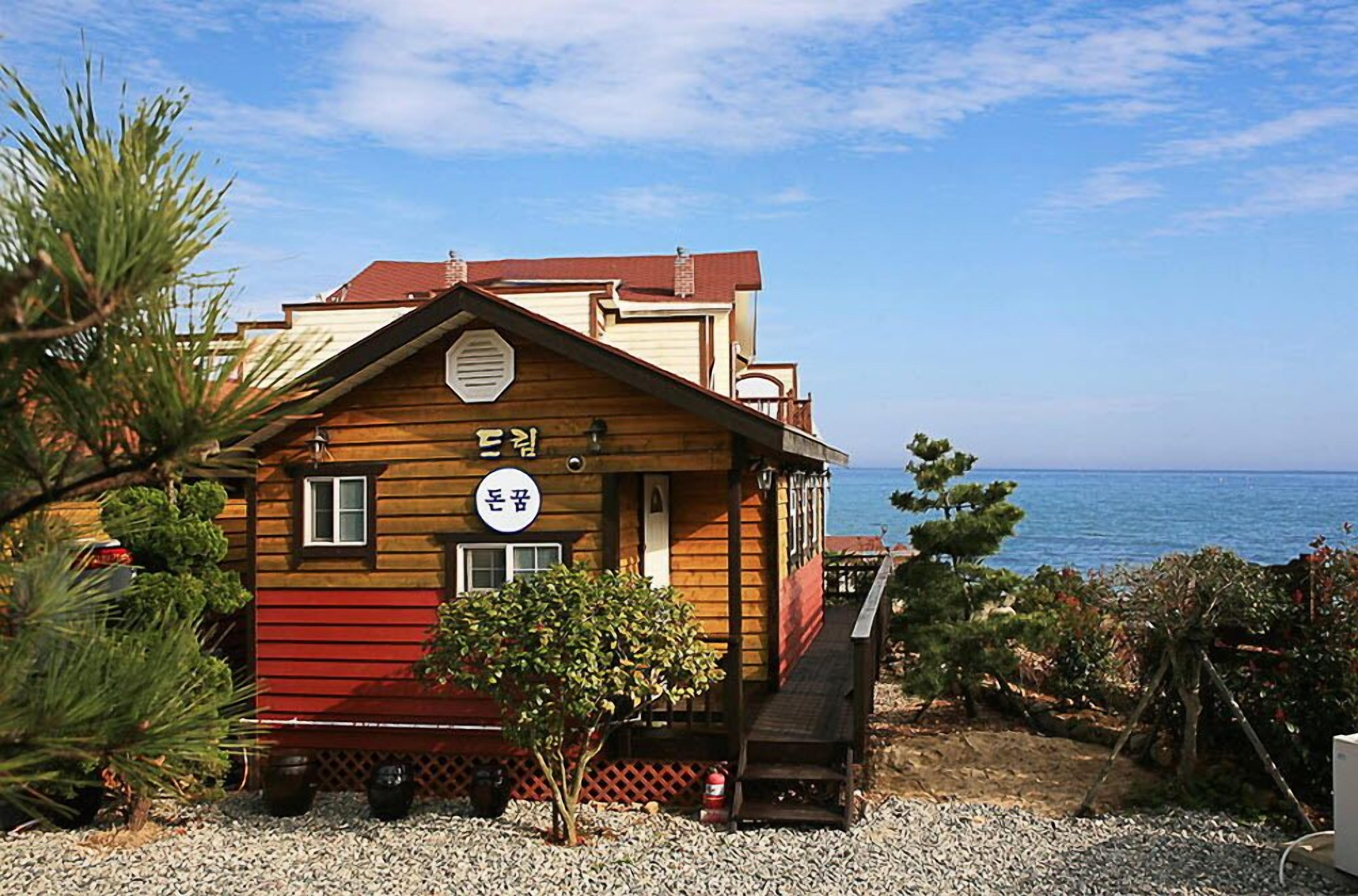 A wooden building with a red lower section and a balcony, located near a body of water.