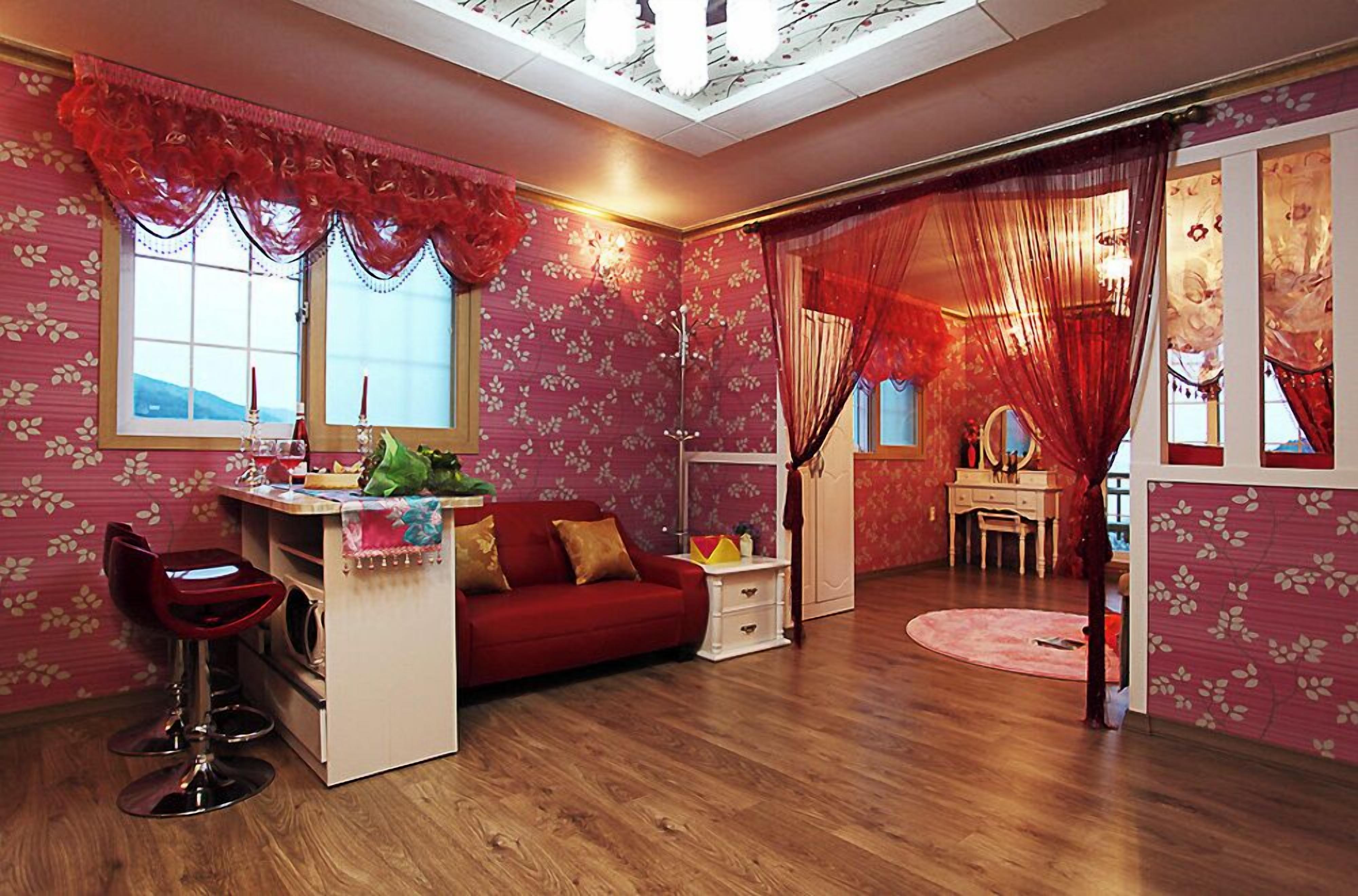 A room with a red sofa, a desk with a chair, and a vanity with a mirror.