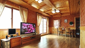 Un interior de madera con un televisor sobre un mueble de madera, un escritorio con una computadora y una zona de comedor con sillas y una mesa.