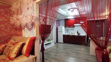 Una sala de estar con un sofá, una cocina al fondo y cortinas rojas.