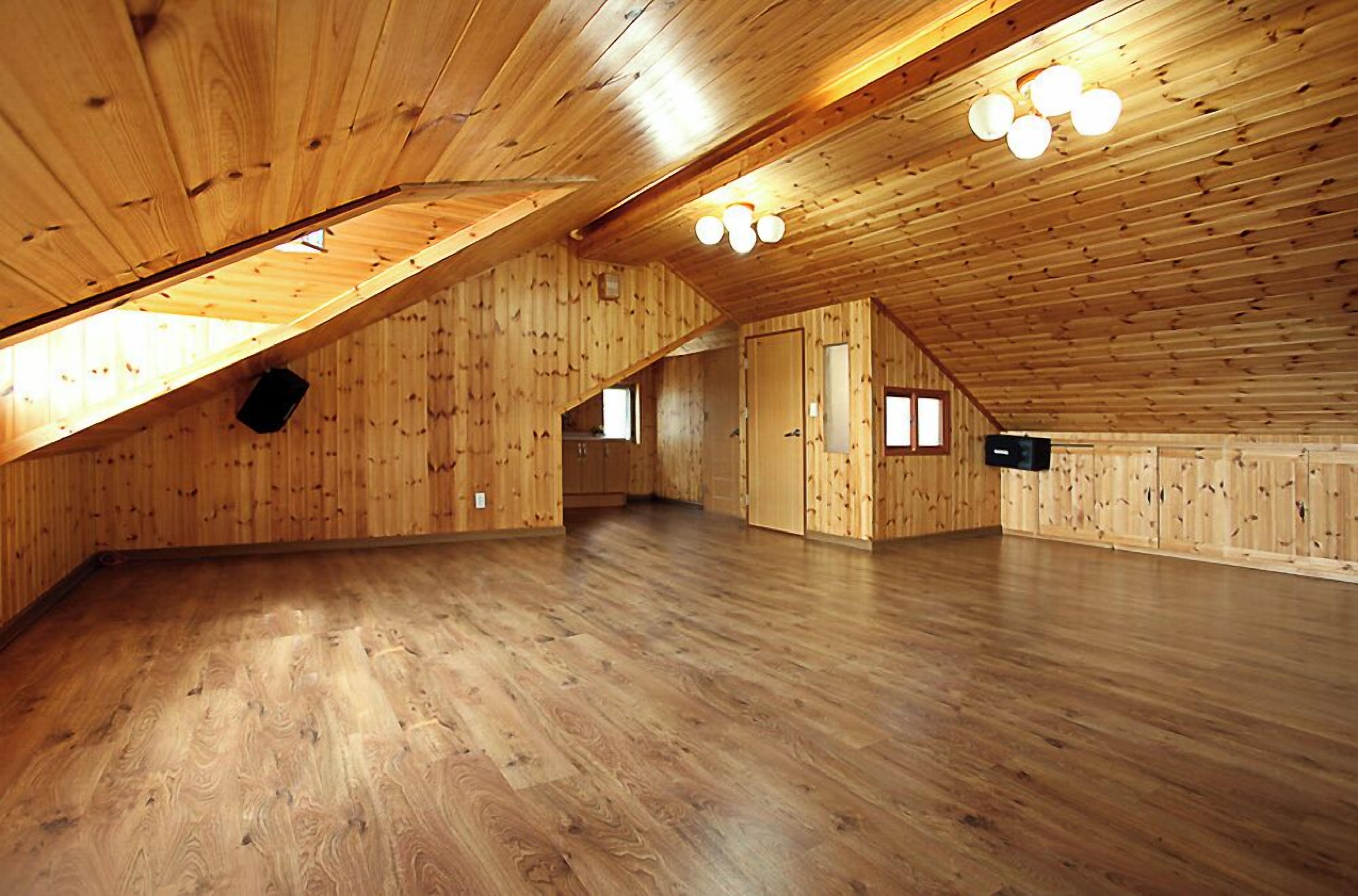 A spacious attic room with wooden walls and floors, a sloped ceiling, and a skylight.
