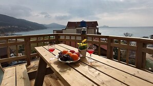 Terraza de madera con una mesa dispuesta para dos personas, con frutero y dos vasos de bebida roja.