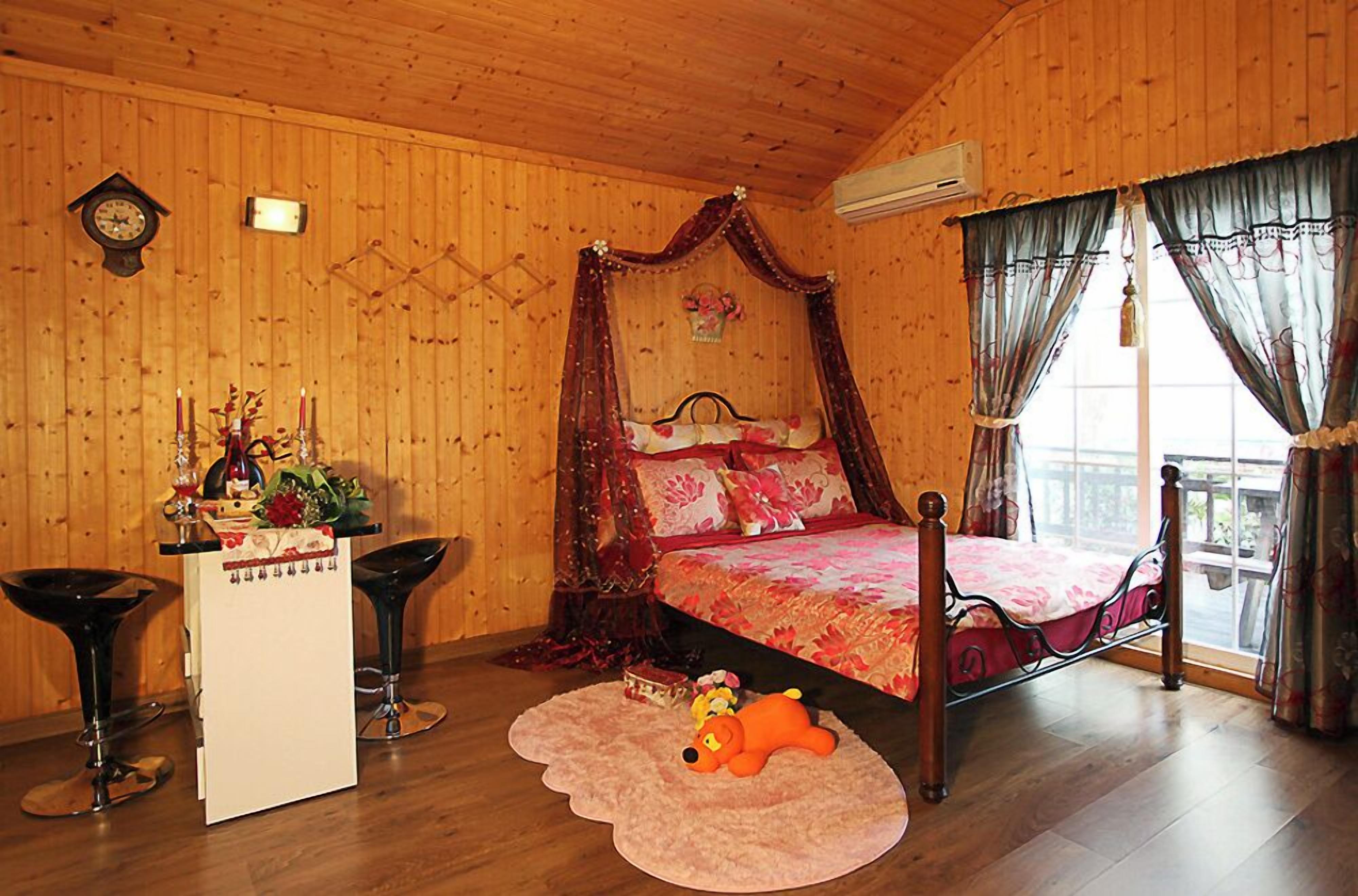 Une pièce en bois avec un lit, un bureau, deux chaises, une horloge et une fenêtre avec des rideaux.