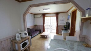 A cozy room with a wooden ceiling, a sofa, a dining table, and a kitchen area. - Haemaru pension (Geoje)