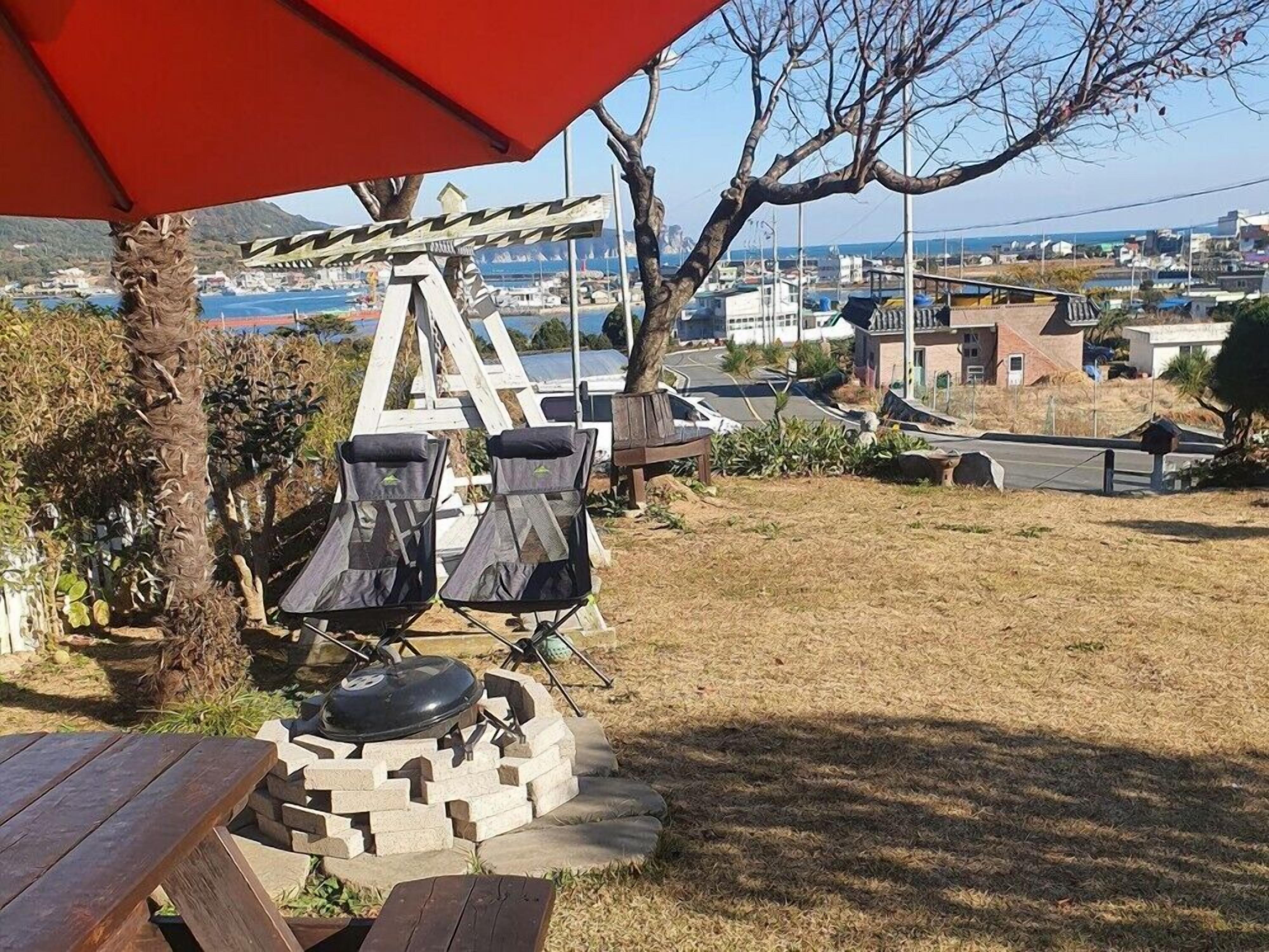 Un patio con una parrilla, dos sillas y un paraguas rojo.