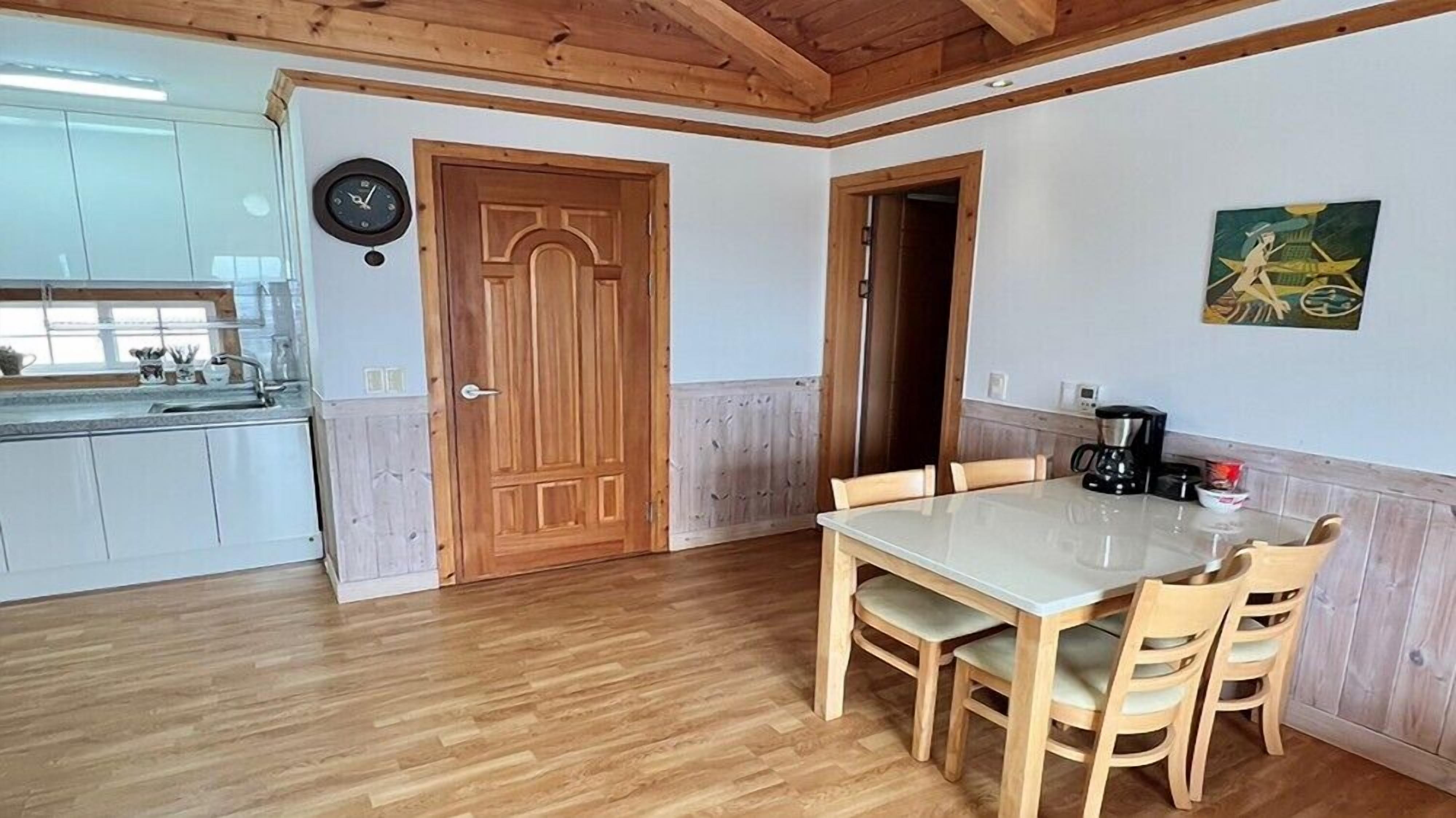 Ett kök med träskåp, ett matbord med stolar, en klocka på väggen och en tavla.