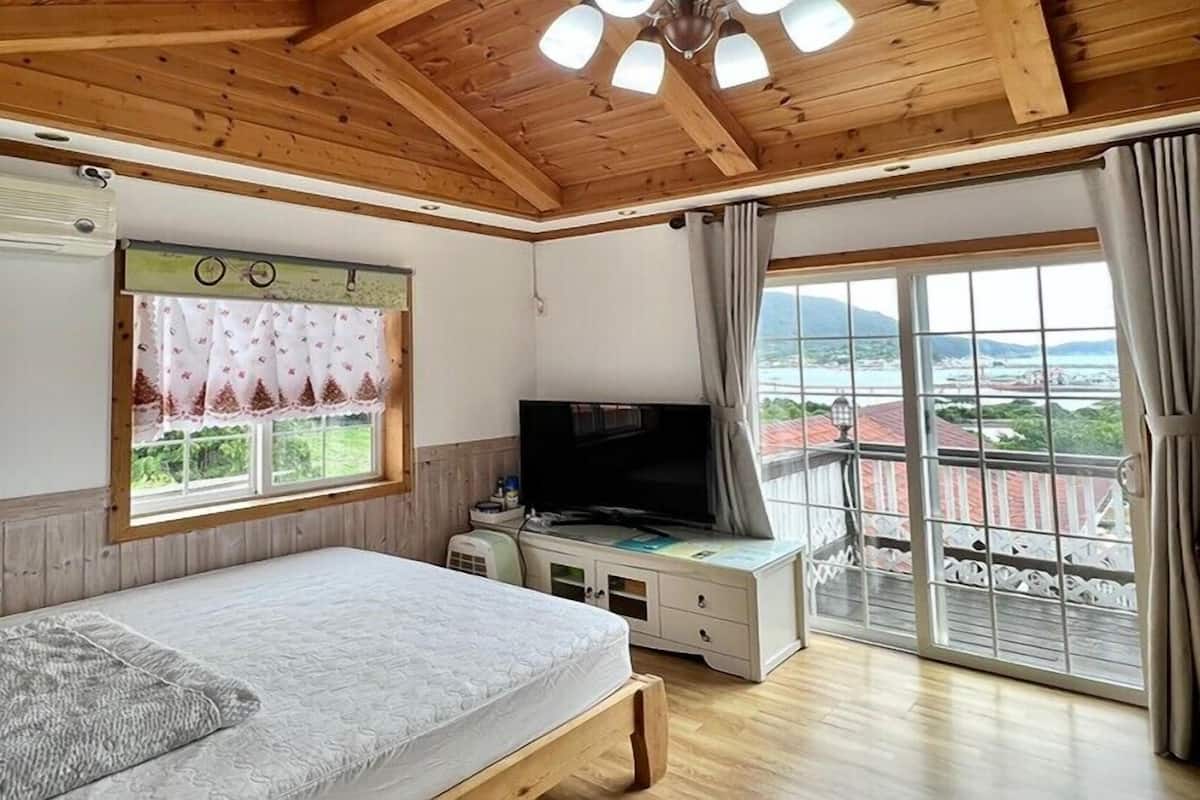 Un dormitorio con cama, televisión, ventana con cortinas y balcón con vistas.