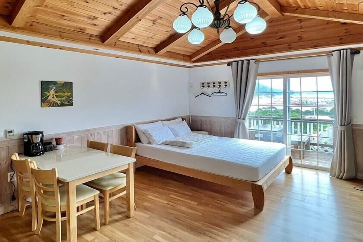 Un dormitorio acogedor con techo de madera, una cama, una mesa de comedor con sillas y vistas de la ciudad a través de amplias ventanas.