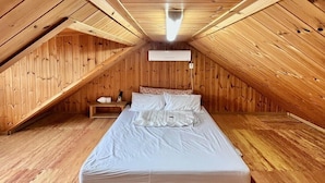 A small, wooden attic bedroom with a single bed, a nightstand, and a wall-mounted air conditioner. - Haemaru pension (Geoje)