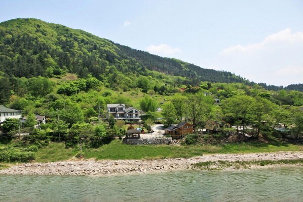 Une propriété située au bord de la rivière, comprenant des maisons, un kiosque et une vue sur les montagnes en arrière-plan.