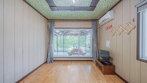 Una habitación con suelo de madera, un ventanal con cortinas, un ventilador de techo y aire acondicionado instalado.