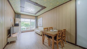 Una habitación con piso de madera, una mesa de comedor con sillas, un sofá, un televisor y una ventana con vista a la vegetación.