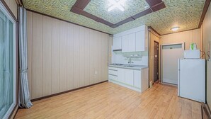 Una cocina compacta con suelo de madera, armarios blancos y un refrigerador pequeño.