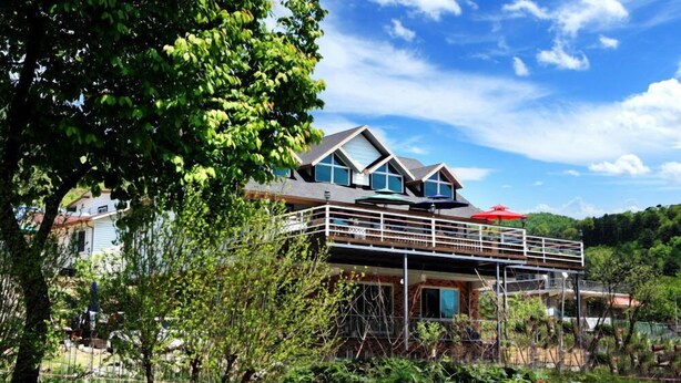 Een modern huis met twee verdiepingen en een balkon, omringd door groen en een heldere lucht.