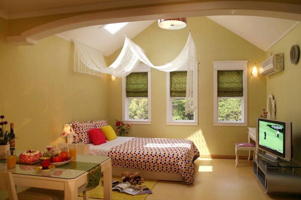 Un dormitorio con cama, televisor, una mesa con desayuno y ventana con cortinas.