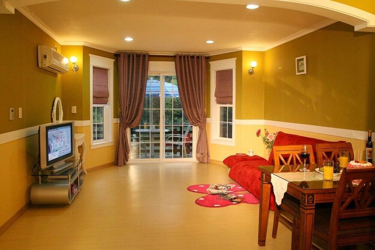 Una sala de estar con televisor, una mesa de comedor con sillas, un sofá rojo y una ventana con cortinas.
