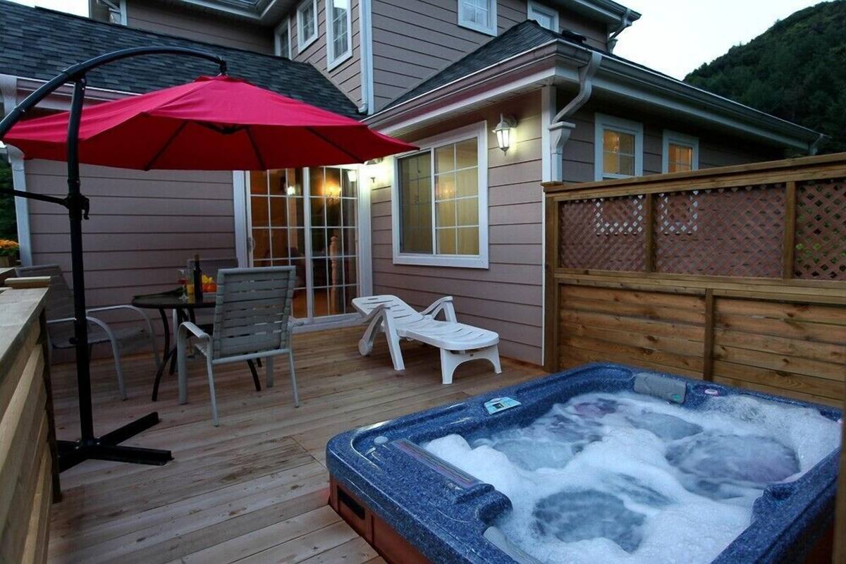 Una terraza de madera con un jacuzzi, sillas de descanso y un paraguas rojo.