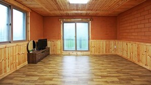 A room with wooden walls and ceiling, a large sliding glass door, and a wooden entertainment unit with a television. - Utbeodeong Pension (Chuncheon)