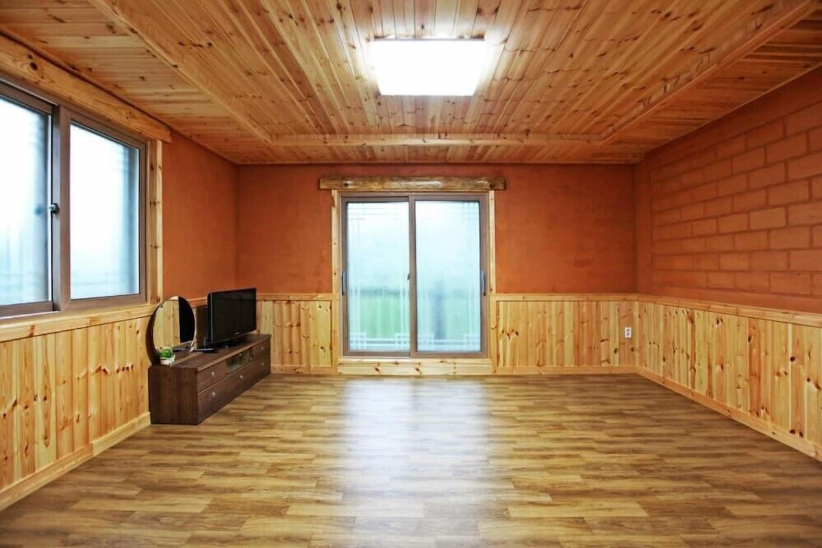A room with wooden walls and ceiling, a large sliding glass door, and a wooden entertainment unit with a television.
