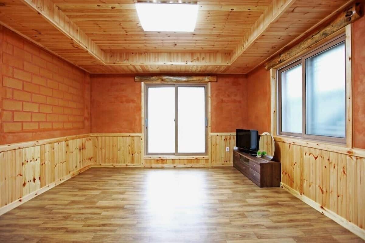 A room with wooden walls and floors, a large sliding glass door, a flat-screen TV, and a wooden dresser.