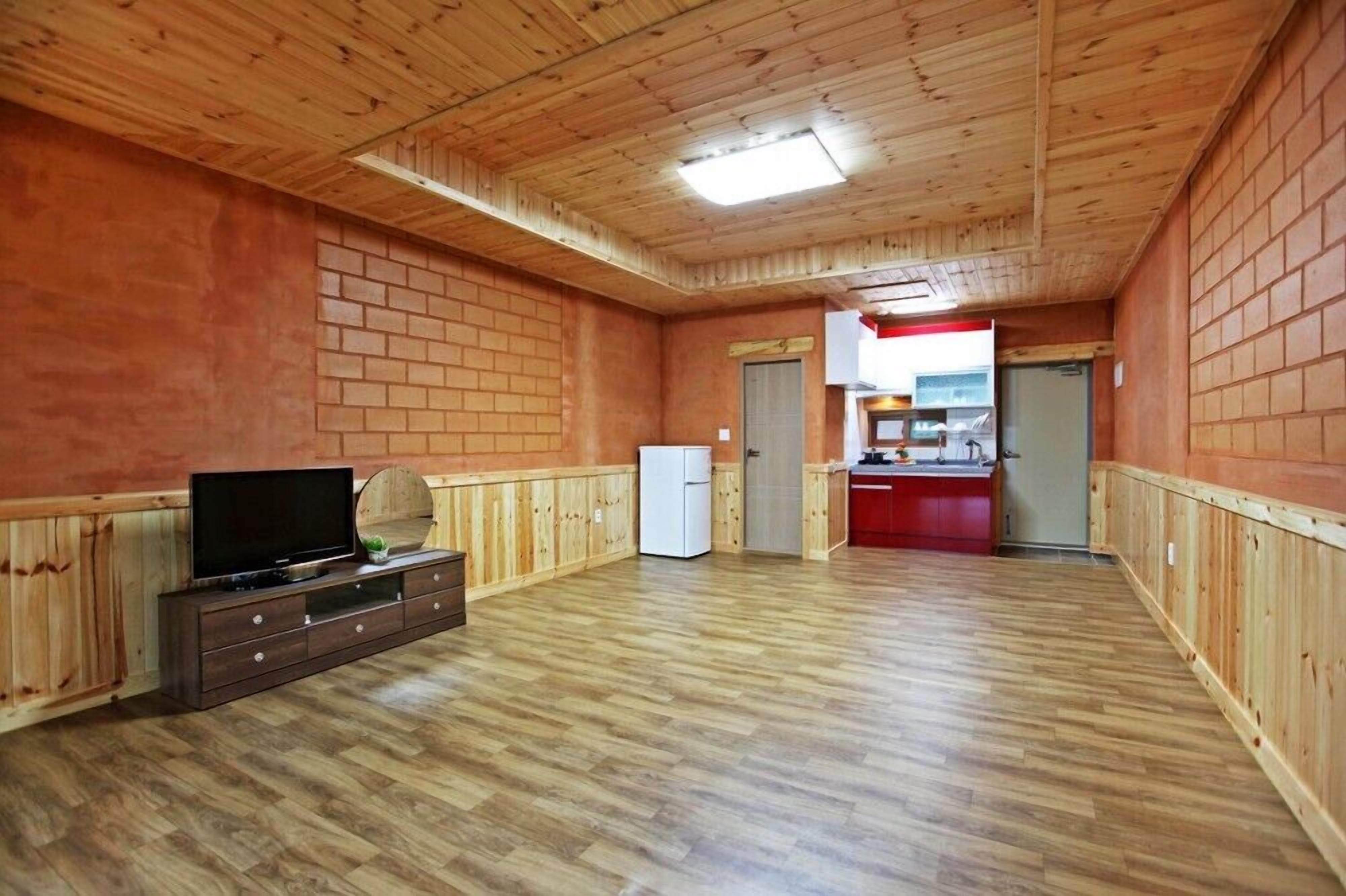 Ein geräumiges Zimmer mit Holzwänden und -boden, einem Fernseher auf einer Holzkommode und einem Kühlschrank.