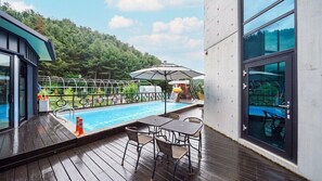 A poolside area with a wooden deck, a pool, and a glass-enclosed patio. - Asamo poolvilla (Gapyeong)