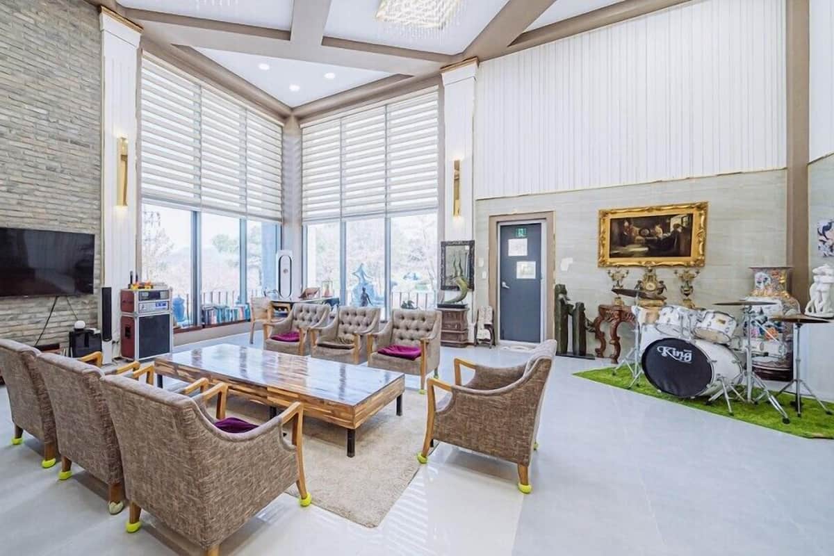 A spacious living room with a large wooden table, comfortable seating, a television, and a drum set.