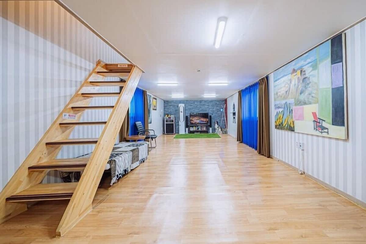 A long, narrow room with a wooden staircase on one side, a flat-screen TV, and a painting on the wall.