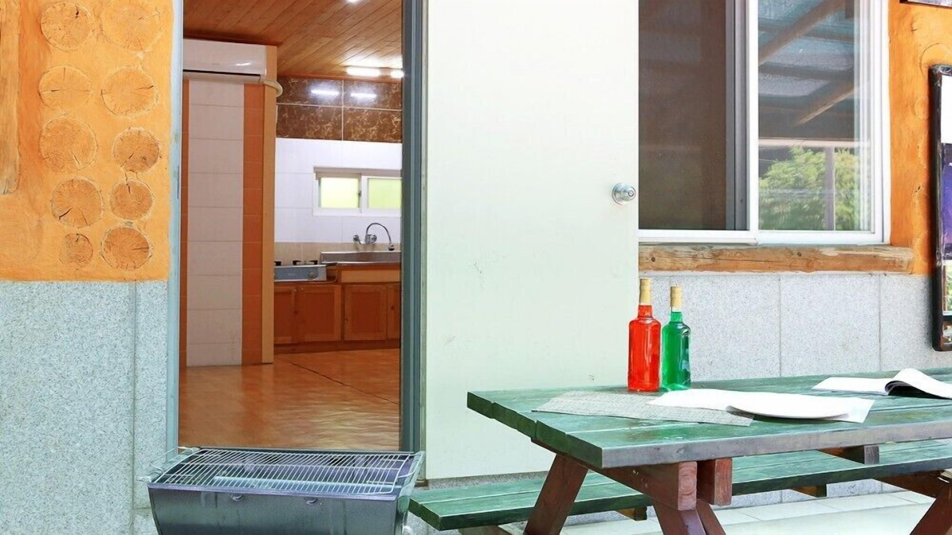 A kitchen with a window, a wooden table with papers, and two bottles on the windowsill.