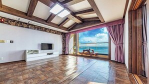 Une pièce spacieuse dotée d’un plancher en bois, d’un téléviseur à écran plat, d’un mur décoratif en pierre et d’une grande fenêtre offrant une vue sur la mer.